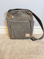 Front view showing gray canvas, leather trim, front zip pockets, Travelon patch, adjustable strap