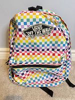 Front view of Vans rainbow checkerboard backpack with logo patch and front zip pocket visible
