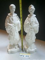 Front view of both white ceramic figurines with tape measure showing height