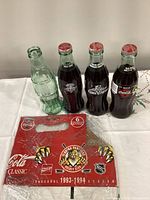 Four commemorative 8oz Coca-Cola glass bottles and red Florida Panthers carry case displayed on table