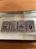 Front view of four chrome flip-top lighters with team crests