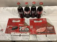 Front view of four commemorative Coca-Cola bottles and two cardboard carriers