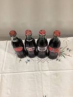 Front view of four sealed commemorative Coca-Cola bottles showing team logos and cap condition