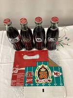 Front view of four sealed commemorative Coca-Cola bottles and Chiefs carrier panel