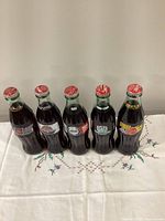 Front view of five sealed 8oz Coca-Cola commemorative bottles showing labels and caps