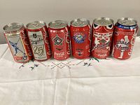 Frontal group shot of all six commemorative Coca-Cola cans listed.