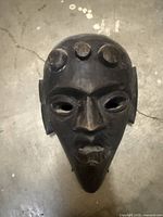 Front view of carved dark wood mask showing facial features and forehead bosses