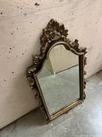 Front view of ornate gold-tone framed mirror leaning against wall