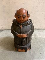 Front view of hand-sculpted terracotta monk figurine showing facial features, robe, cross and paint wear