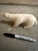 Side view of marble polar bear beside marker for scale