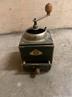 Front view showing grinder body, crank, drawer and logo