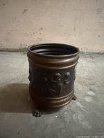 Front view of embossed copper container showing relief figures and feet