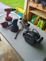 Overall view of drill, sander, routers, inspection camera, battery and ratchet on table