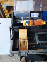 Toolbox open showing rope roll, drill bit set in wooden case, assorted hand tools