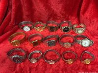 Fifteen assorted wristwatches displayed on red fabric showing cases and bracelets