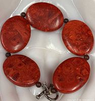 Bracelet laid flat showing five oval red coral beads, round spacers, toggle clasp
