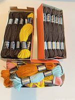 Three boxes of DMC wool skeins showing brown, yellow, orange, pink, blue colors