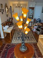 Full view of lamp on table showing height, all eight lit shades, bronze floral base