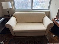 Front view of beige upholstered convertible sofa under window, shows overall design and upholstery condition.