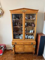 Full view of cabinet showing glass doors, pediment top, mounts and lower storage