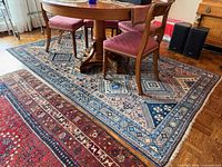 Full view of blue Persian rug under dining table with fringe and patterned borders