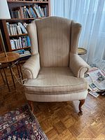 Front view of beige striped wingback chair showing upholstery, arms, legs, cushion