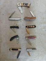 Group shot of nine folding knives laid out on fabric