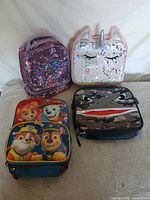 Group shot of two backpacks (purple sequin, PAW Patrol) and two lunch bags (pink unicorn, camo shark)