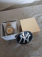 Watch in Michael Kors box next to belt buckle front view