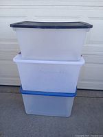 Stack of three clear plastic storage totes with black, white and blue lids shown together