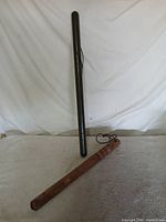 Two vintage law-enforcement implements: painted weighted rod standing, wood baton lying