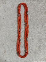 Full view of entire multi-strand orange seed bead necklace laid flat