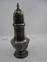 Full view of metal sugar caster showing octagonal base, faceted body and pierced domed top with finial
