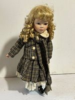 Front view of DSN porcelain doll in plaid outfit on stand