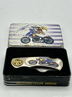 Knife in open tin showing handle artwork and emblem