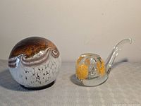 Overview of both art glass pieces: spherical paperweight and clear pipe sculpture
