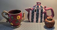 Group shot showing striped ceramic teapot, red sunflower planter and carved wooden vase