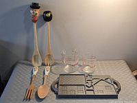 All items laid out: cast iron mold, two Fire-King cups, two long novelty wooden servers, two ceramic-handled utensils