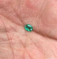 Oval green emerald on fingertip showing size and facets
