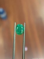 Front view of oval emerald held by tweezers
