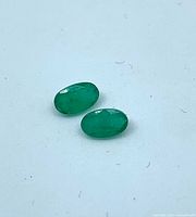 Pair of green oval cabochon emeralds on white background