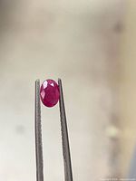 Ruby held in gem tweezers showing shape and facets