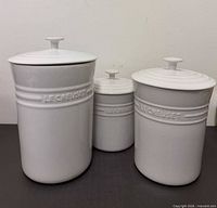 Front view of three white Le Creuset stoneware canisters with lids
