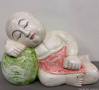 Front view of carved wooden sleeping baby Buddha resting on green pumpkin