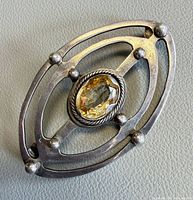 Front view of sterling silver brooch showing openwork frame, central faceted light yellow gemstone, and ball accents