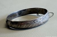 Entire bangle angled view showing etched floral design and safety chain