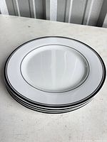 Stack of four matching white plates with black rim lines