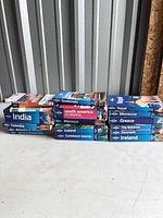 Two horizontal stacks of Lonely Planet and Time Out travel guide books on white surface