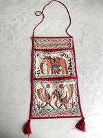 Full view of embroidered wall hanging showing overall design, pockets, cord, tassels