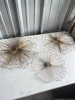 Three gold metal wire floral wall decor pieces on table